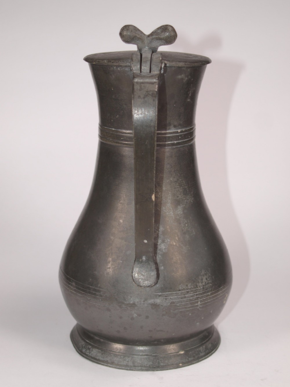 An antique dark grey pewter lidded flagon featuring a bulbous body, flared collar, hinged lid, and handle. View V
