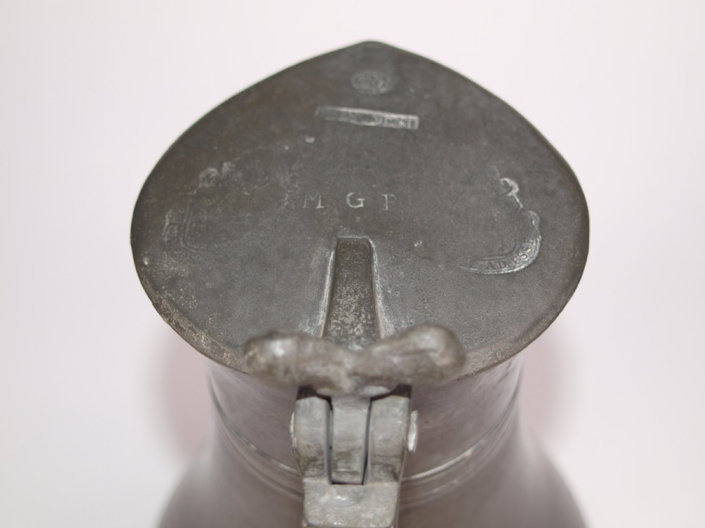 An antique dark grey pewter lidded flagon featuring a bulbous body, flared collar, hinged lid, and handle. View VII