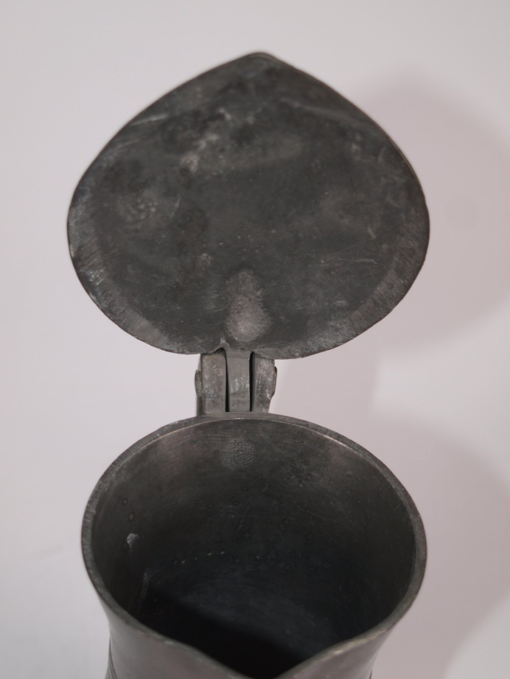 An antique dark grey pewter lidded flagon featuring a bulbous body, flared collar, hinged lid, and handle. View XII