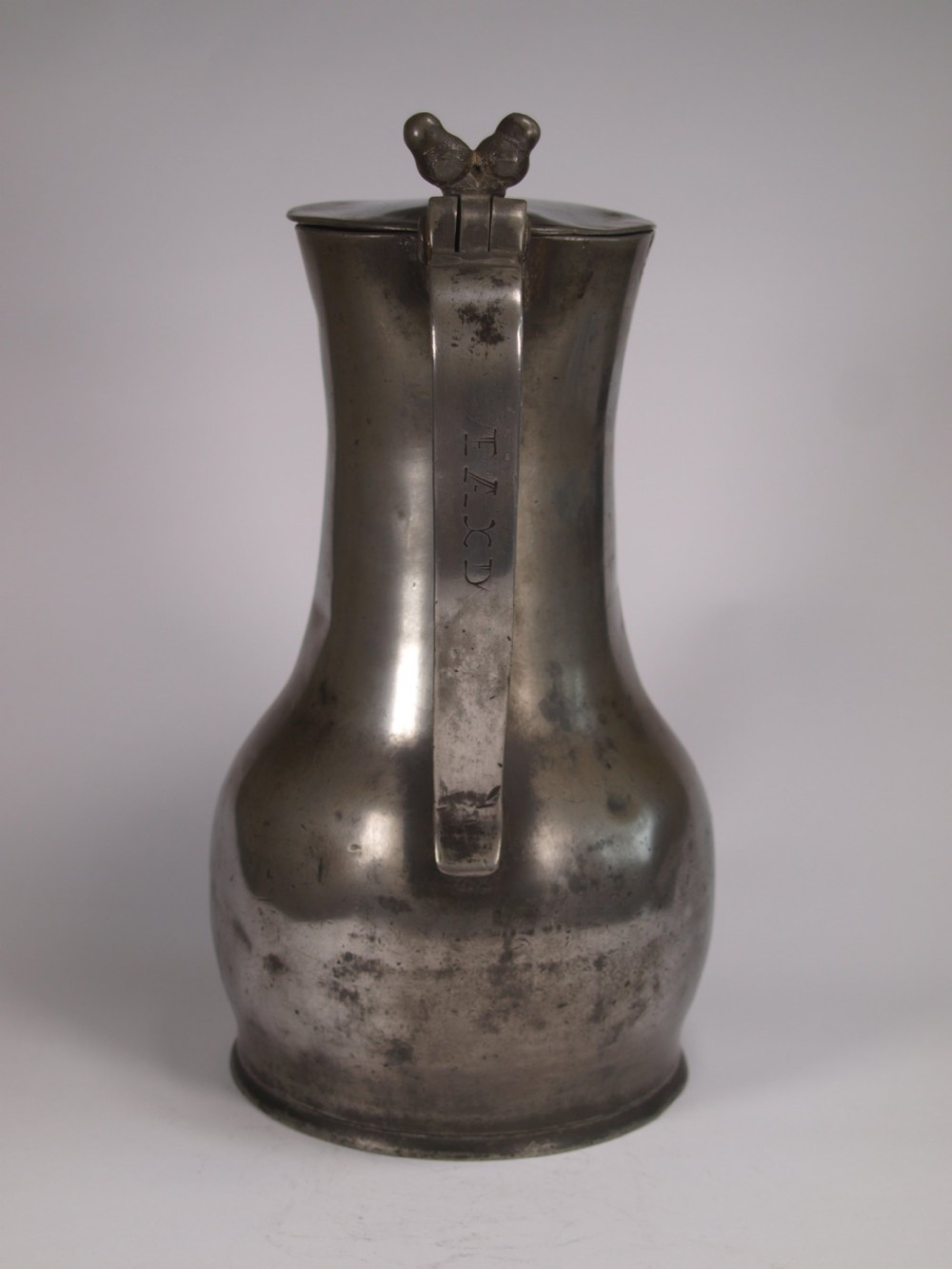 An antique pewter Jersey measure with a hinged lid, double acorn thumbpiece, curved handle, and bulbous body. View II