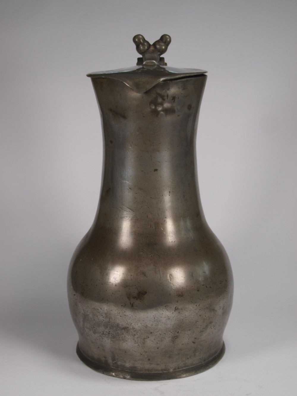 An antique pewter Jersey measure with a hinged lid, double acorn thumbpiece, curved handle, and bulbous body. View V