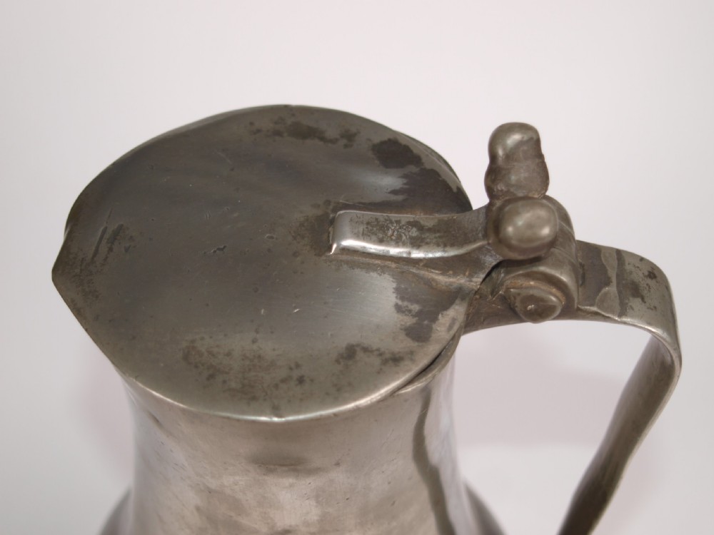 An antique pewter Jersey measure with a hinged lid, double acorn thumbpiece, curved handle, and bulbous body. View VI