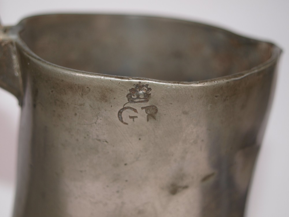 An antique pewter Jersey measure with a hinged lid, double acorn thumbpiece, curved handle, and bulbous body. View IX