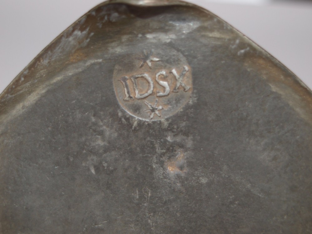 An antique pewter Jersey measure with a hinged lid, double acorn thumbpiece, curved handle, and bulbous body. View X