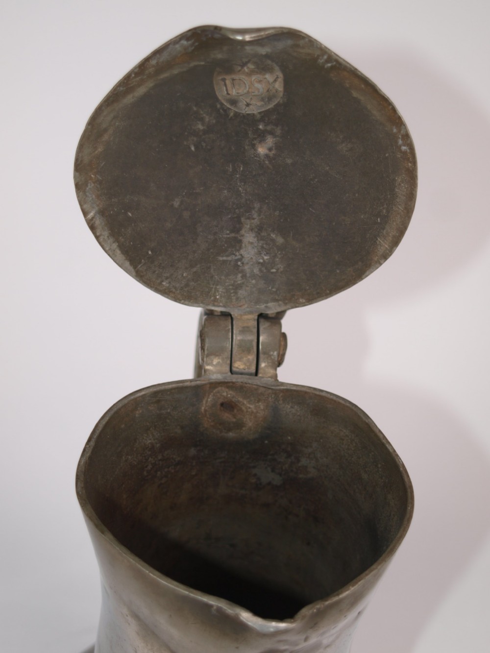 An antique pewter Jersey measure with a hinged lid, double acorn thumbpiece, curved handle, and bulbous body. View XII