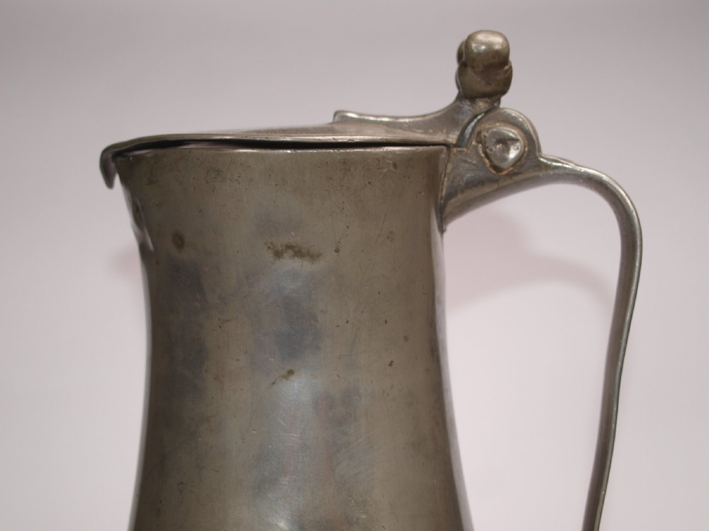 An antique pewter Jersey measure with a hinged lid, double acorn thumbpiece, curved handle, and bulbous body. View XIII