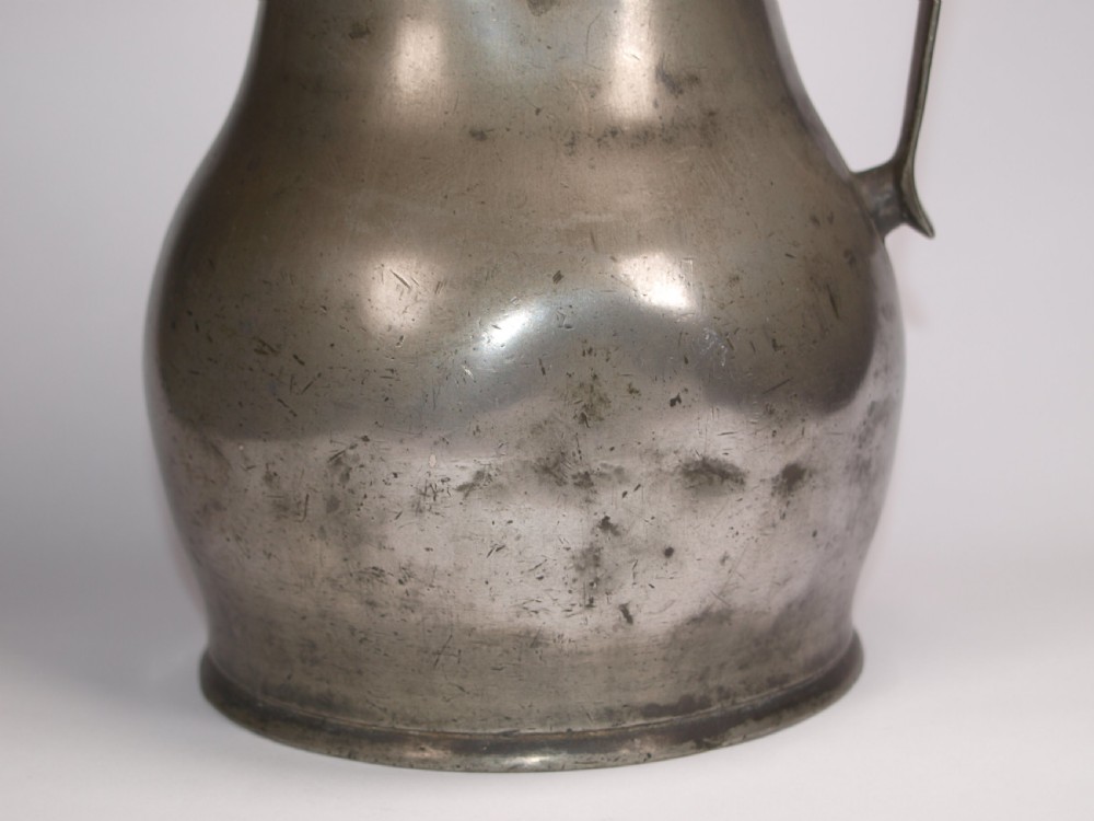 An antique pewter Jersey measure with a hinged lid, double acorn thumbpiece, curved handle, and bulbous body. View XIV