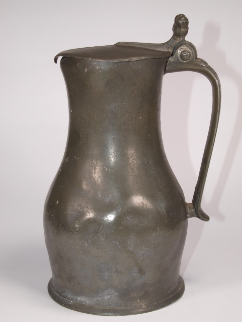 An antique slate grey pewter lidded quart measure featuring a baluster shape, attached strap handle, and hinged lid.