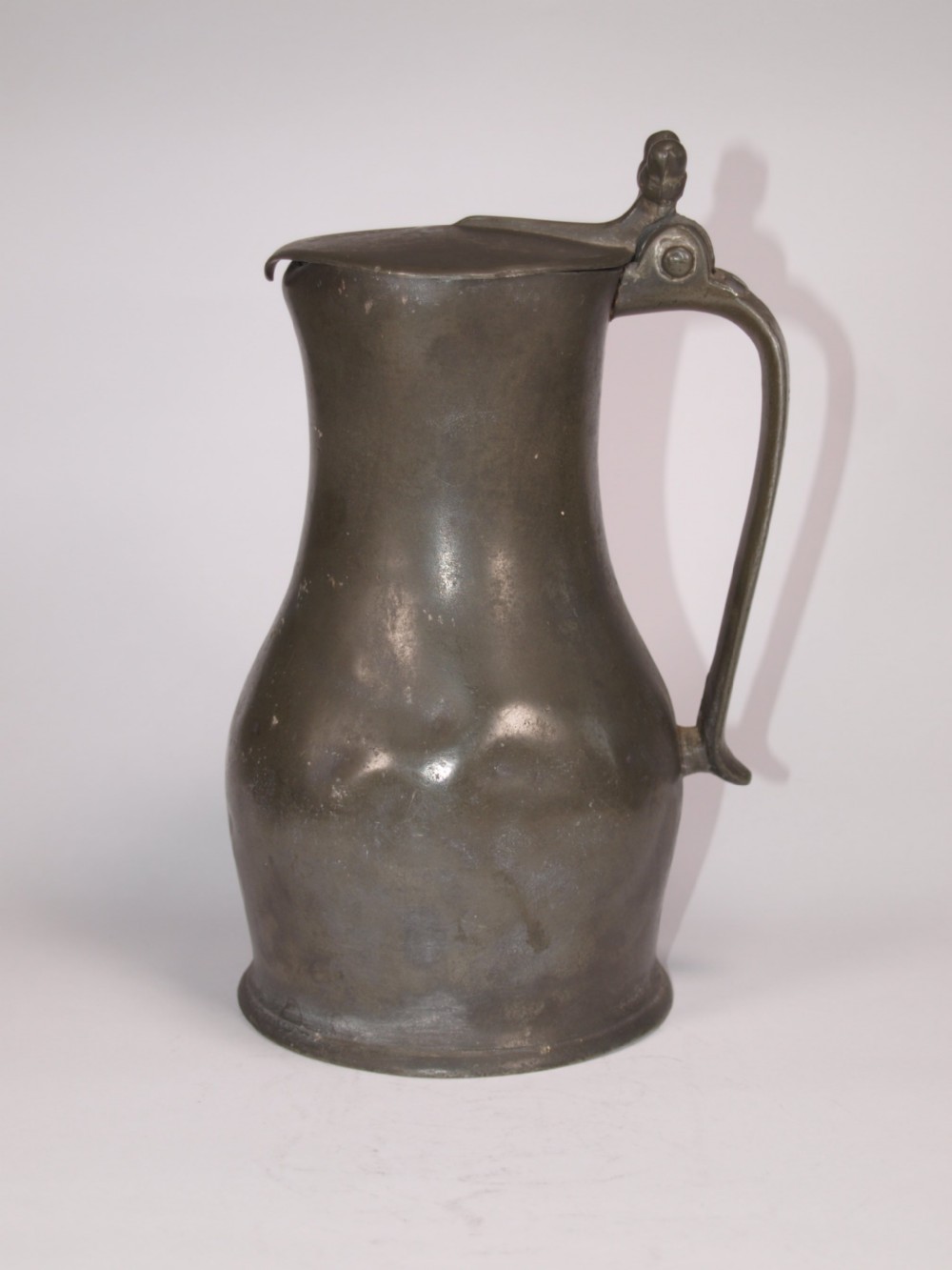 An antique slate grey pewter lidded quart measure featuring a baluster shape, attached strap handle, and hinged lid. View VI