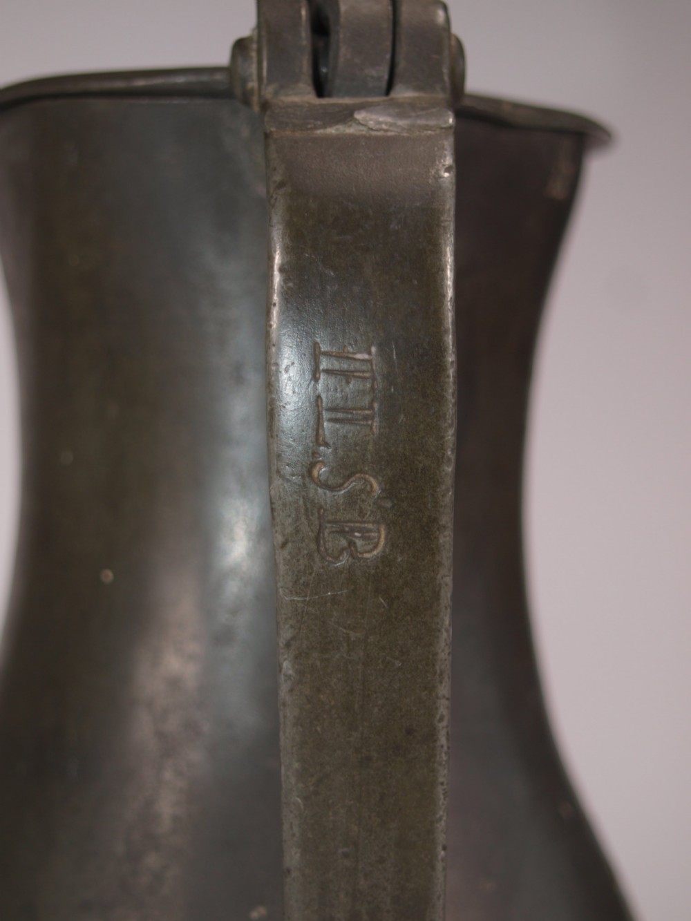 An antique slate grey pewter lidded quart measure featuring a baluster shape, attached strap handle, and hinged lid. View X