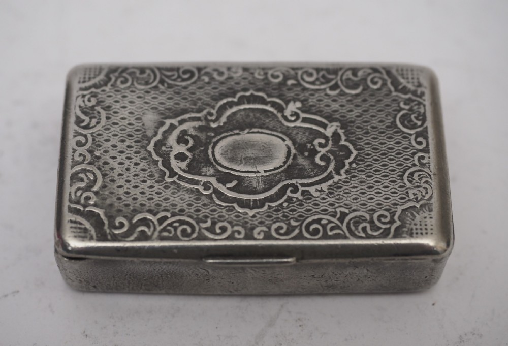 A rectangular antique pewter snuff box featuring an engraved central cartouche surrounded by scrollwork and textured engine-turned patterning.