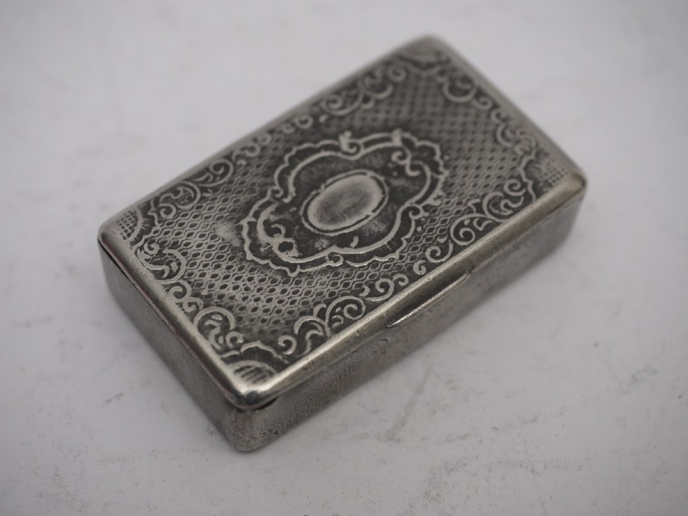 A rectangular antique pewter snuff box featuring an engraved central cartouche surrounded by scrollwork and textured engine-turned patterning. View II