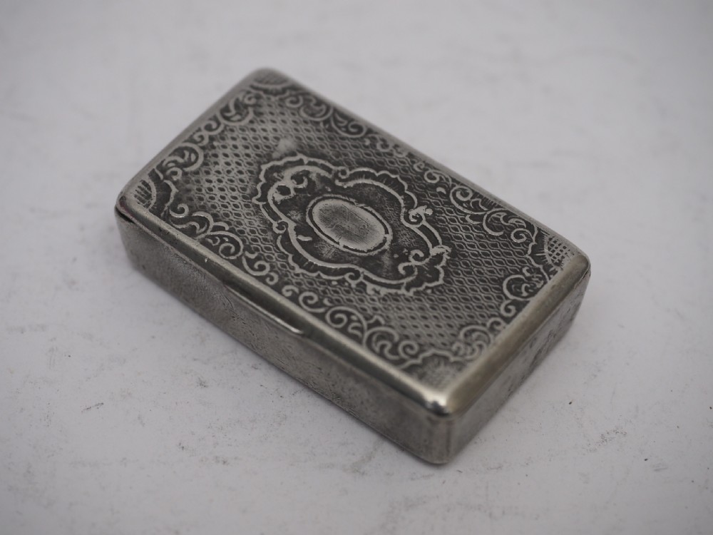 A rectangular antique pewter snuff box featuring an engraved central cartouche surrounded by scrollwork and textured engine-turned patterning. View III