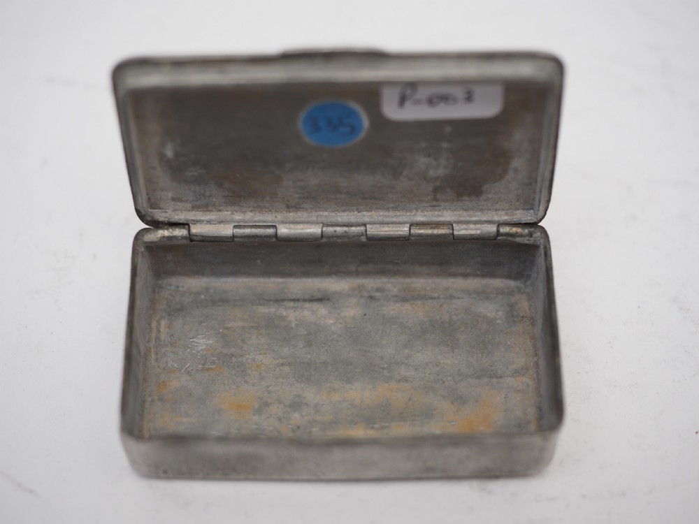 A rectangular antique pewter snuff box featuring an engraved central cartouche surrounded by scrollwork and textured engine-turned patterning. View V