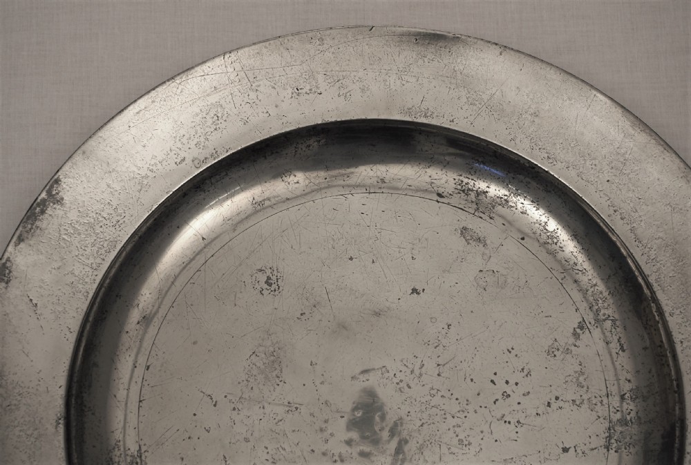 A circular 18th-century English pewter charger featuring a broad plain rim and an aged patinated surface. View II