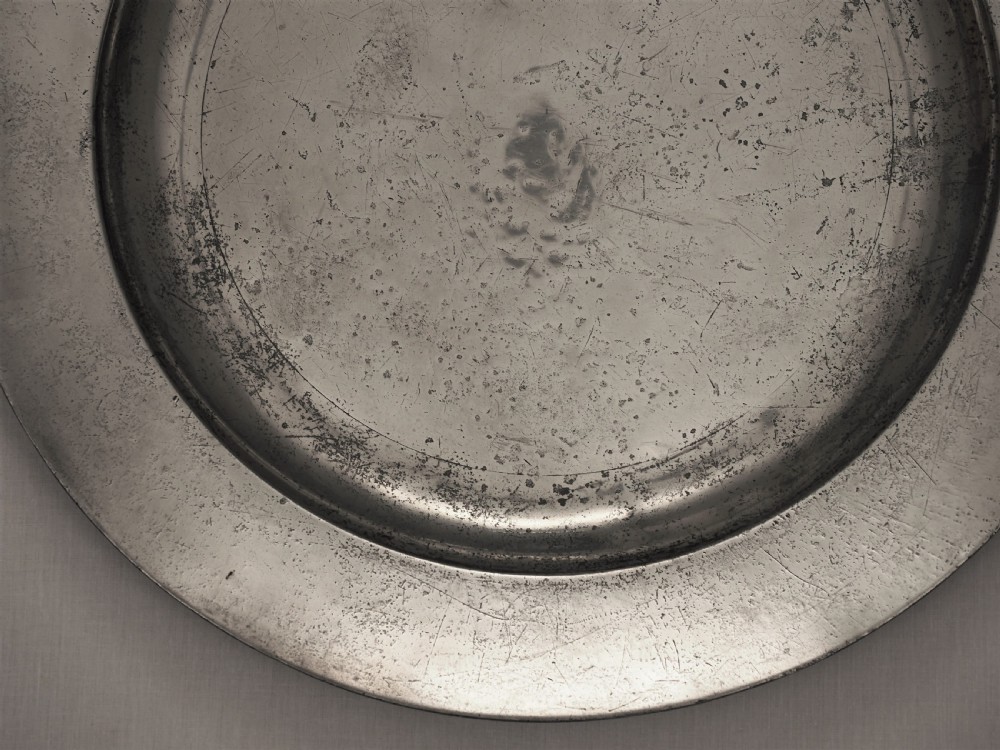 A circular 18th-century English pewter charger featuring a broad plain rim and an aged patinated surface. View III