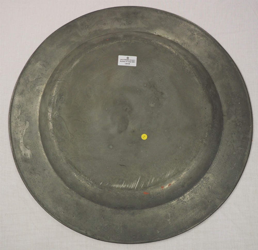 A circular antique grey pewter charger plate featuring a wide rim with reeded moulding and stamped maker touchmarks along the upper edge. View II