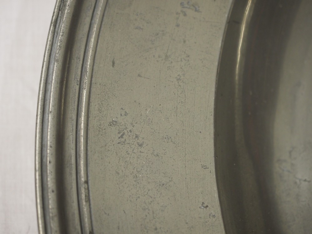 A circular antique grey pewter charger plate featuring a wide rim with reeded moulding and stamped maker touchmarks along the upper edge. View IV