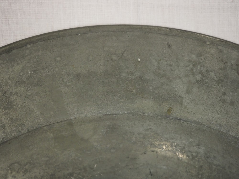 A circular antique grey pewter charger plate featuring a wide rim with reeded moulding and stamped maker touchmarks along the upper edge. View VII