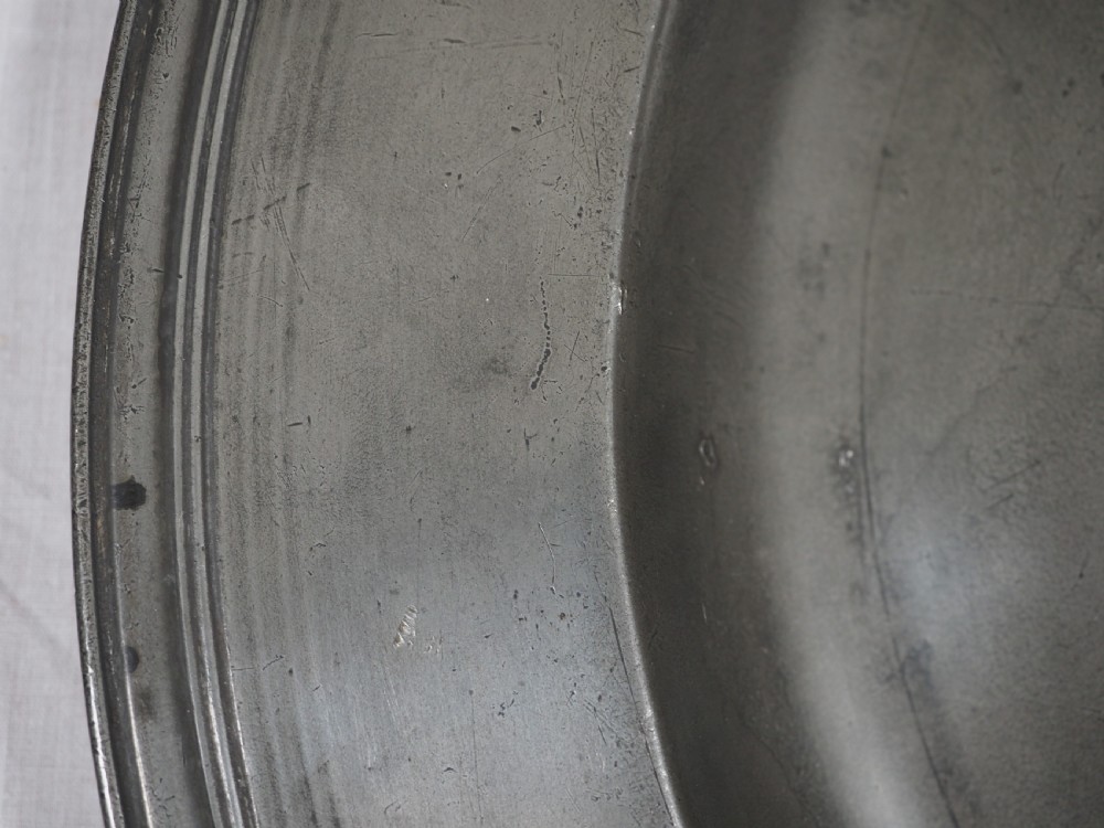 A circular 17th-century pewter charger plate featuring a wide rim decorated with triple reeded moulding and visible maker touchmarks. View II