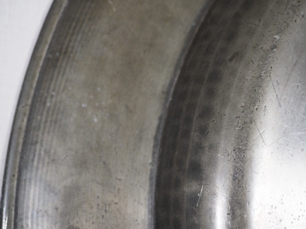 A circular 17th-century pewter charger plate featuring a wide rim decorated with triple reeded moulding and visible maker touchmarks. View VI
