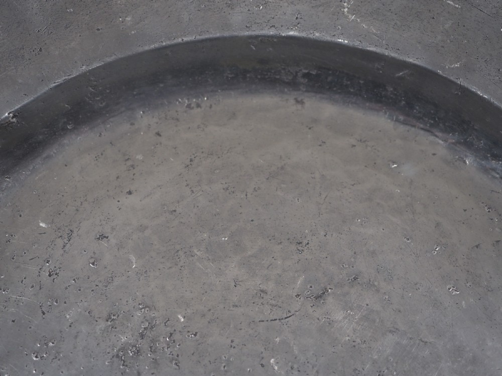 A circular 17th-century English pewter charger featuring a wide flat rim decorated with incised lines and a hand-hammered surface patina. View III