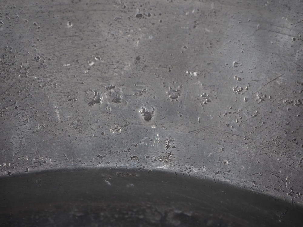 A circular 17th-century English pewter charger featuring a wide flat rim decorated with incised lines and a hand-hammered surface patina. View IV