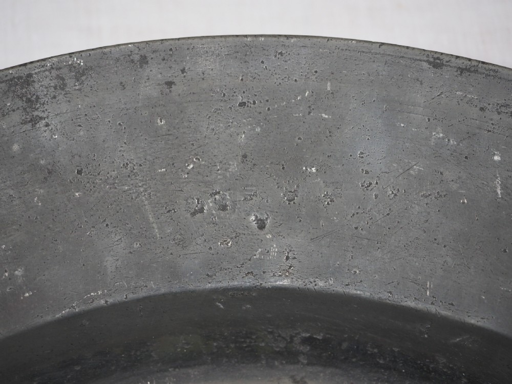 A circular 17th-century English pewter charger featuring a wide flat rim decorated with incised lines and a hand-hammered surface patina. View VI