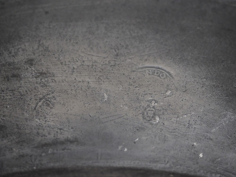 A circular 17th-century English pewter charger featuring a wide flat rim decorated with incised lines and a hand-hammered surface patina. View VIII