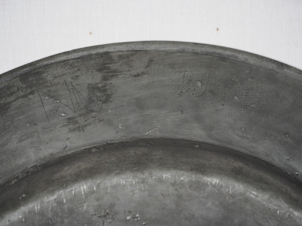A circular 17th-century English pewter charger featuring a wide flat rim decorated with incised lines and a hand-hammered surface patina. View IX