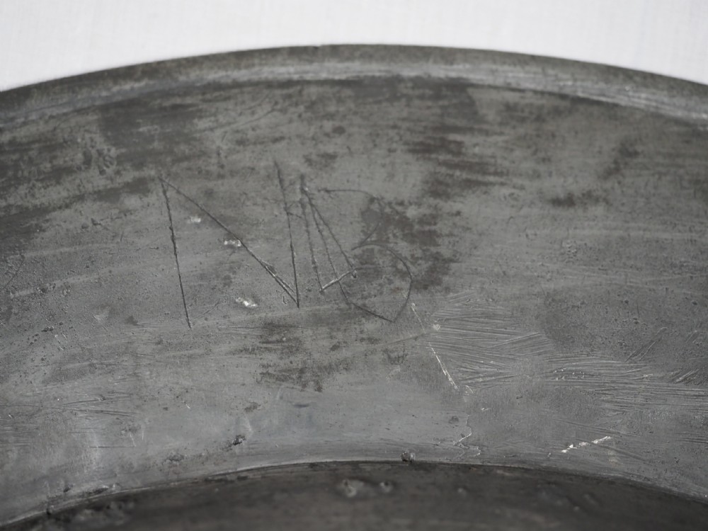 A circular 17th-century English pewter charger featuring a wide flat rim decorated with incised lines and a hand-hammered surface patina. View X
