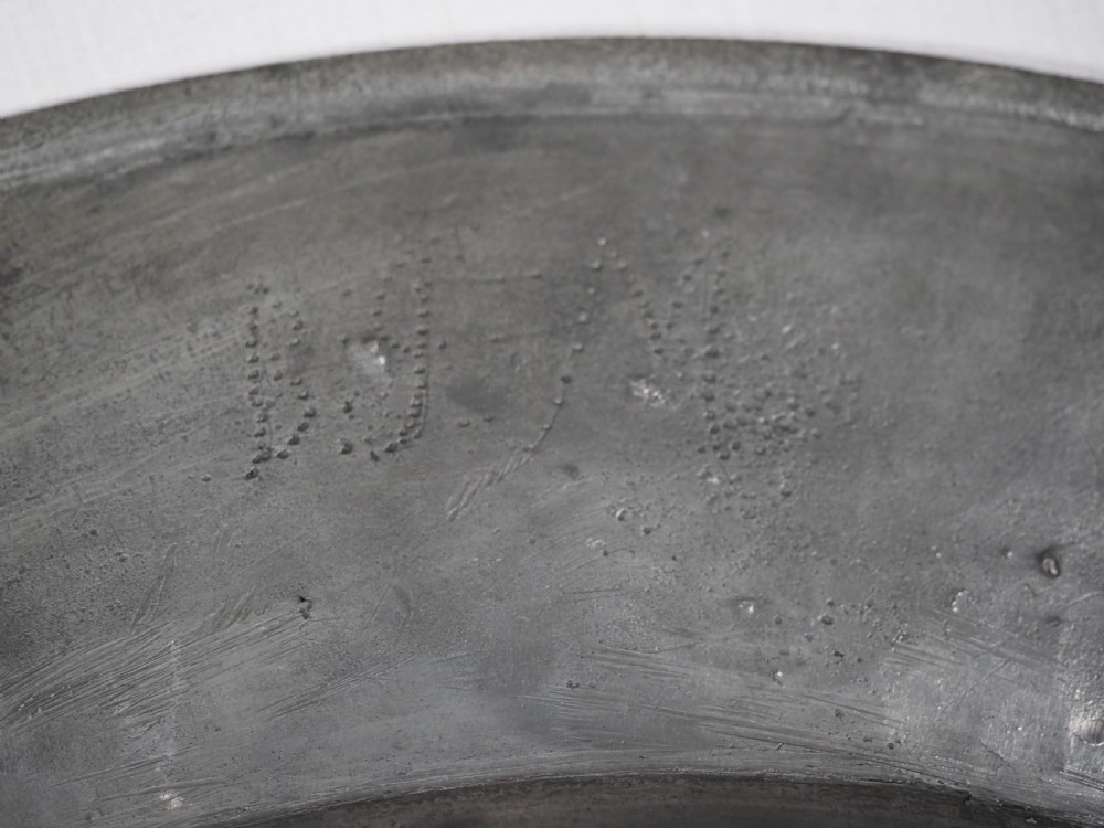 A circular 17th-century English pewter charger featuring a wide flat rim decorated with incised lines and a hand-hammered surface patina. View XI
