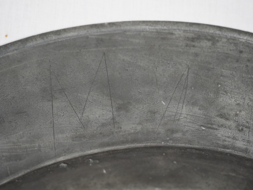 A circular 17th-century English pewter charger featuring a wide flat rim decorated with incised lines and a hand-hammered surface patina. View XII