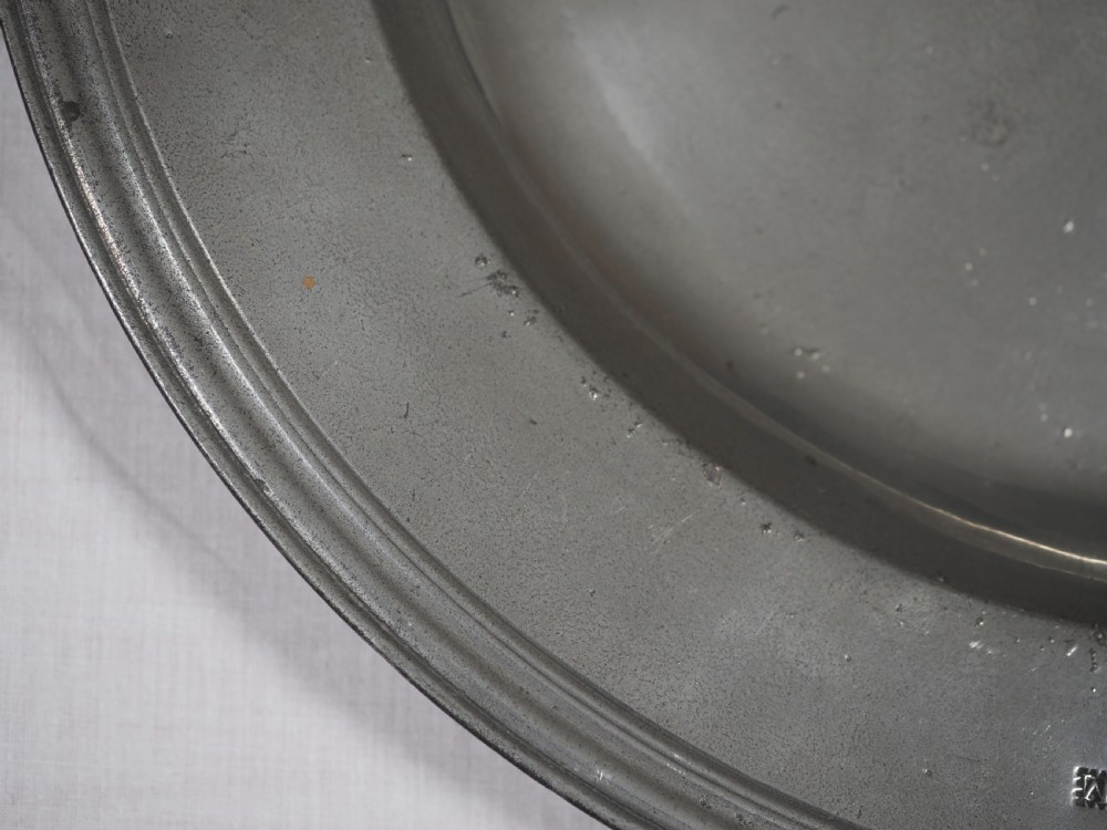 A circular antique English pewter dish featuring a wide rim with multiple reeded edge mouldings and maker touchmarks visible on the lower brim. View II