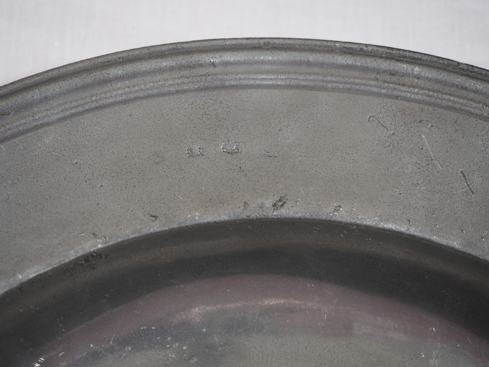A circular antique English pewter dish featuring a wide rim with multiple reeded edge mouldings and maker touchmarks visible on the lower brim. View III