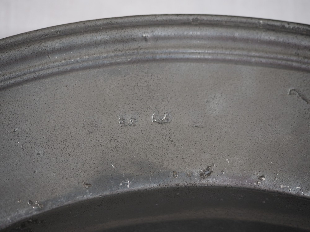 A circular antique English pewter dish featuring a wide rim with multiple reeded edge mouldings and maker touchmarks visible on the lower brim. View IV