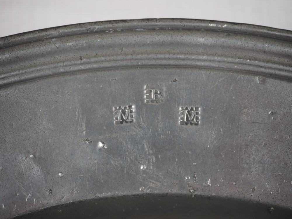A circular antique English pewter dish featuring a wide rim with multiple reeded edge mouldings and maker touchmarks visible on the lower brim. View V