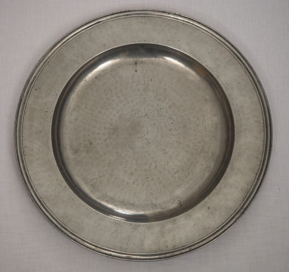 A circular late seventeenth-century grey pewter charger plate featuring a triple-reeded rim and hand-hammered surface finish.
