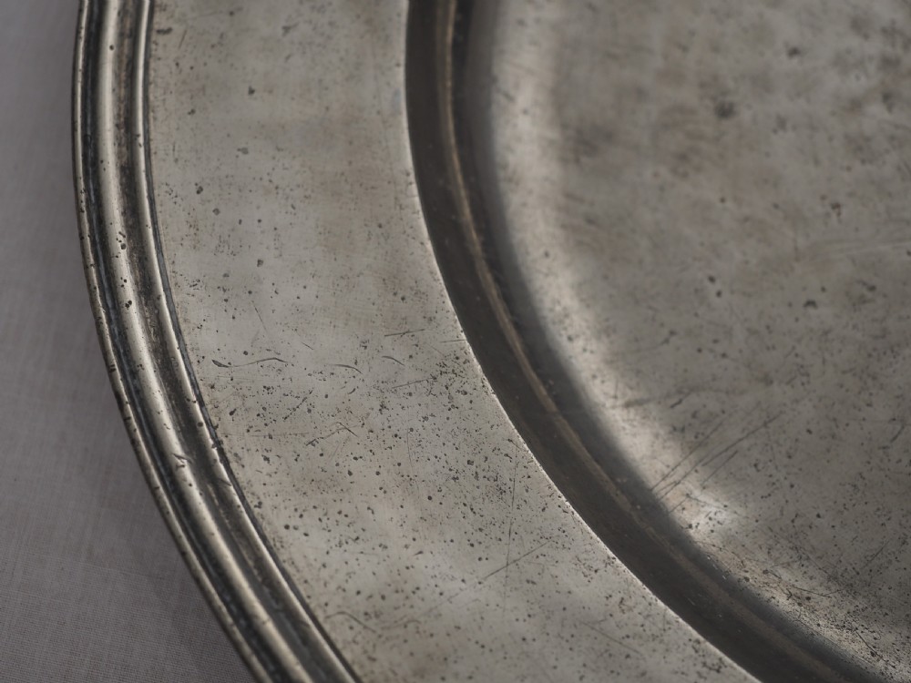A circular late seventeenth-century grey pewter charger plate featuring a triple-reeded rim and hand-hammered surface finish. View III