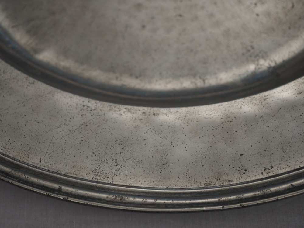 A circular late seventeenth-century grey pewter charger plate featuring a triple-reeded rim and hand-hammered surface finish. View V