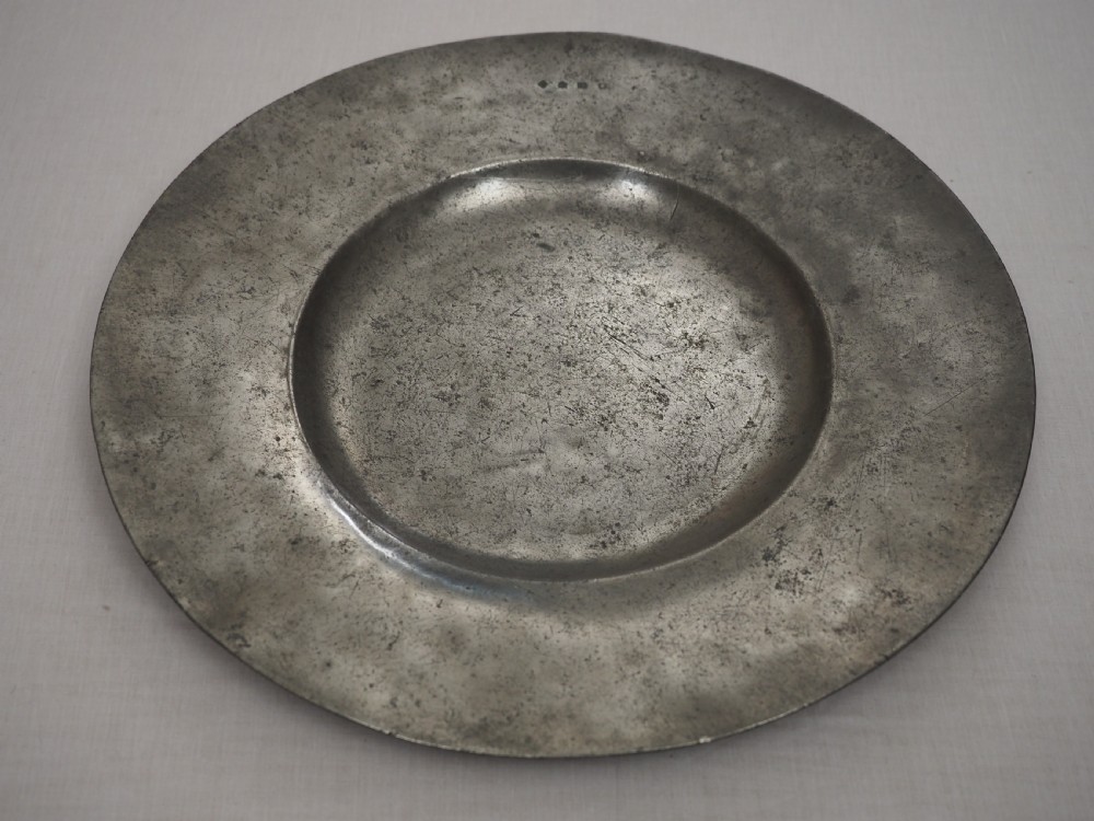 A circular antique pewter charger plate featuring a wide flat rim stamped with hallmarks surrounding a shallow central well. View II