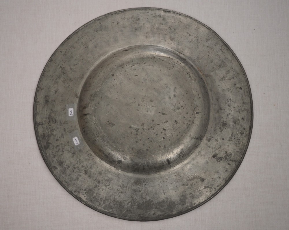 A circular antique pewter charger plate featuring a wide flat rim stamped with hallmarks surrounding a shallow central well. View IV