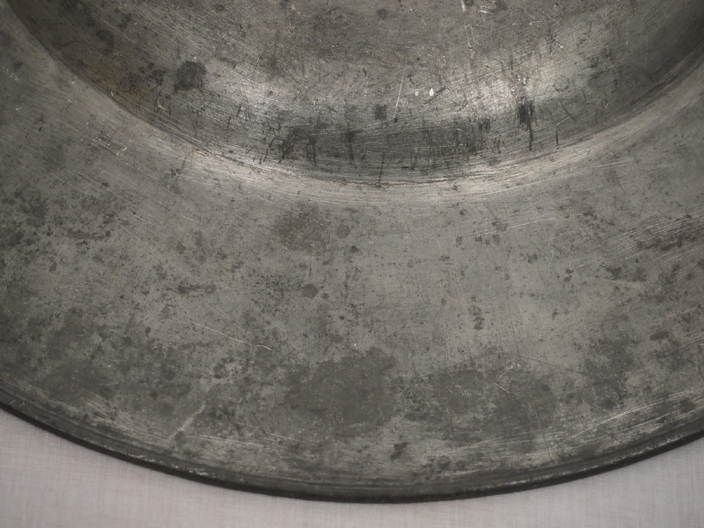 A circular antique pewter charger plate featuring a wide flat rim stamped with hallmarks surrounding a shallow central well. View V
