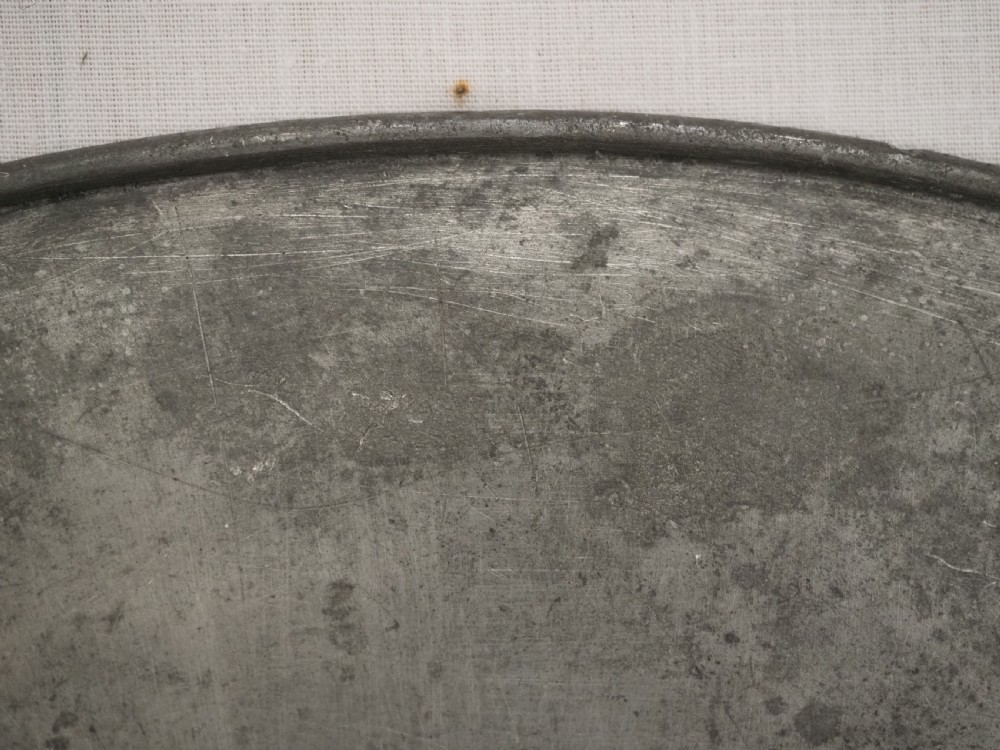 A circular antique pewter charger plate featuring a wide flat rim stamped with hallmarks surrounding a shallow central well. View VI