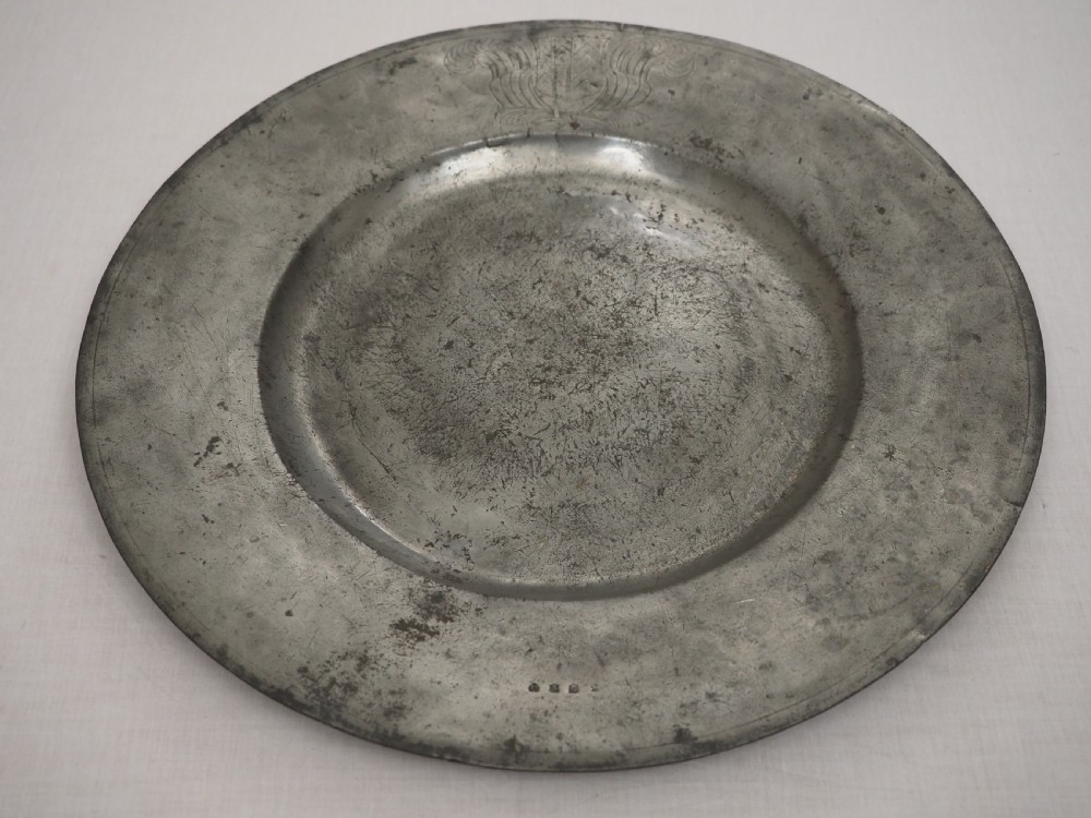 A circular 17th-century pewter charger with a broad rim, featuring an engraved heraldic crest at the top and visible touchmarks at the bottom. View II