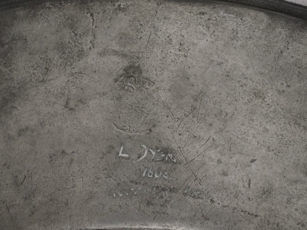 A circular 17th-century pewter charger with a broad rim, featuring an engraved heraldic crest at the top and visible touchmarks at the bottom. View XII
