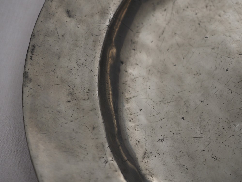 A circular seventeenth-century pewter charger plate with a plain rim featuring an engraved crest and stamped initials. View III