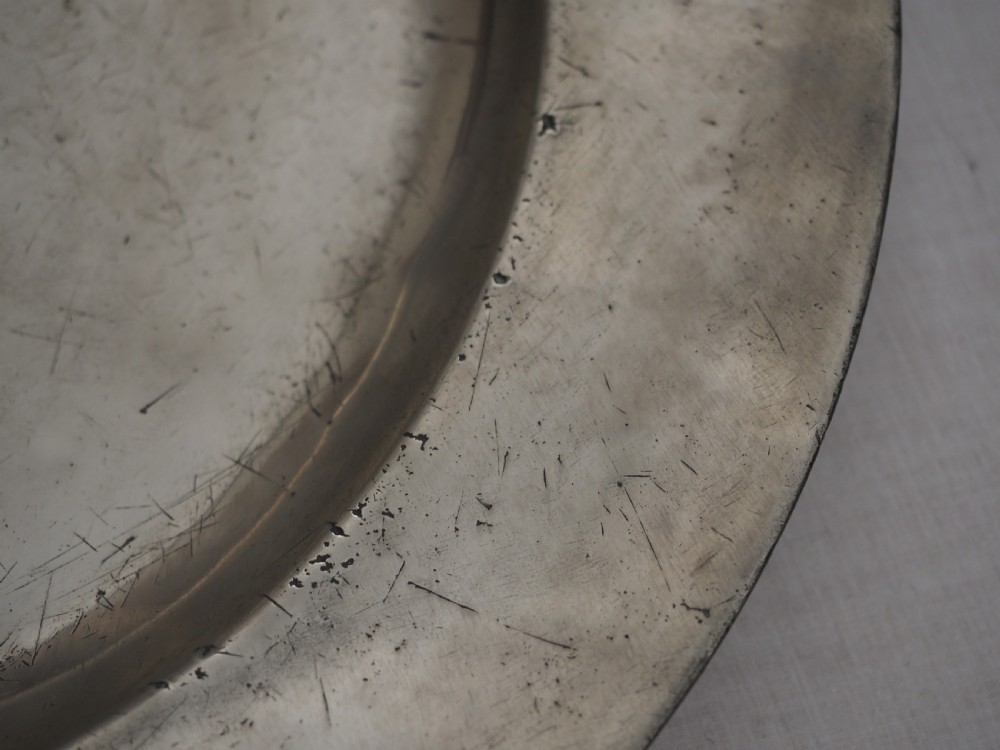 A circular seventeenth-century pewter charger plate with a plain rim featuring an engraved crest and stamped initials. View IV