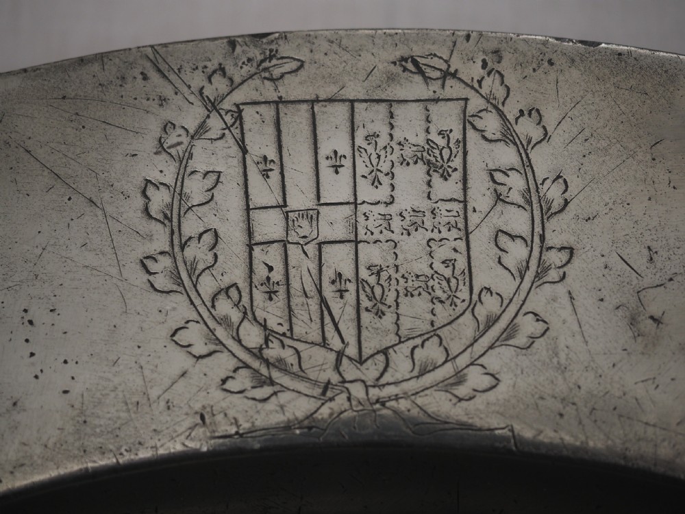 A circular seventeenth-century pewter charger plate with a plain rim featuring an engraved crest and stamped initials. View V