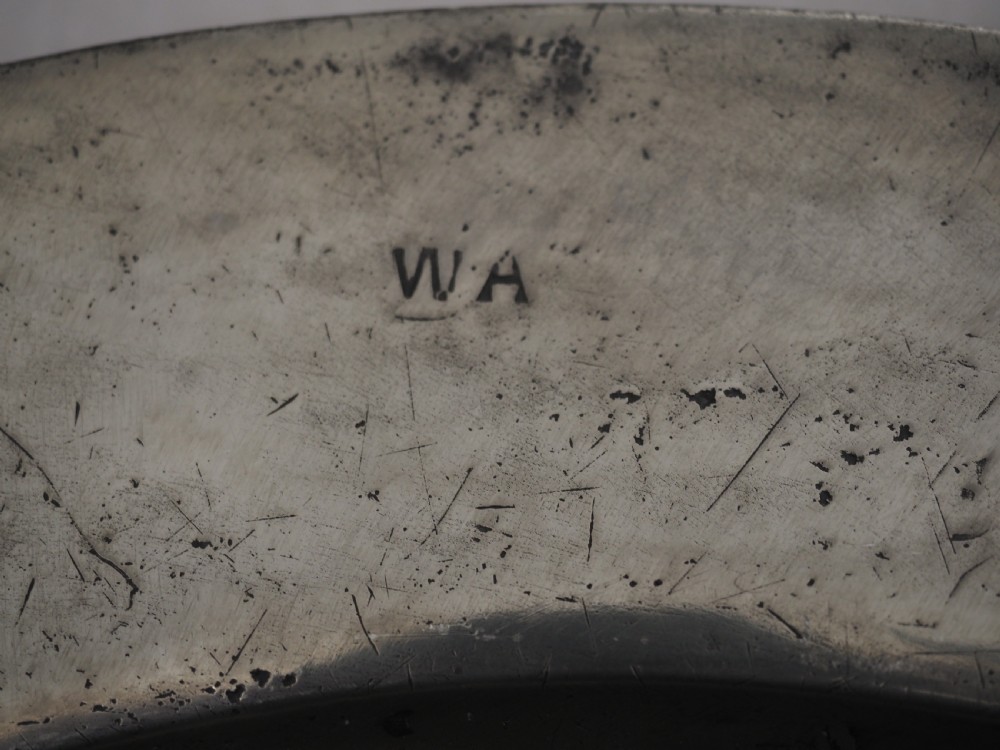 A circular seventeenth-century pewter charger plate with a plain rim featuring an engraved crest and stamped initials. View VI